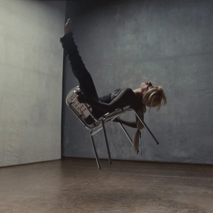 Woman floating mid-air suspended upside down on a metal chair against a textured concrete wall background