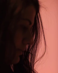 Close-up profile of a woman with long dark hair against a warm pinkish background photographed by Paul Graham