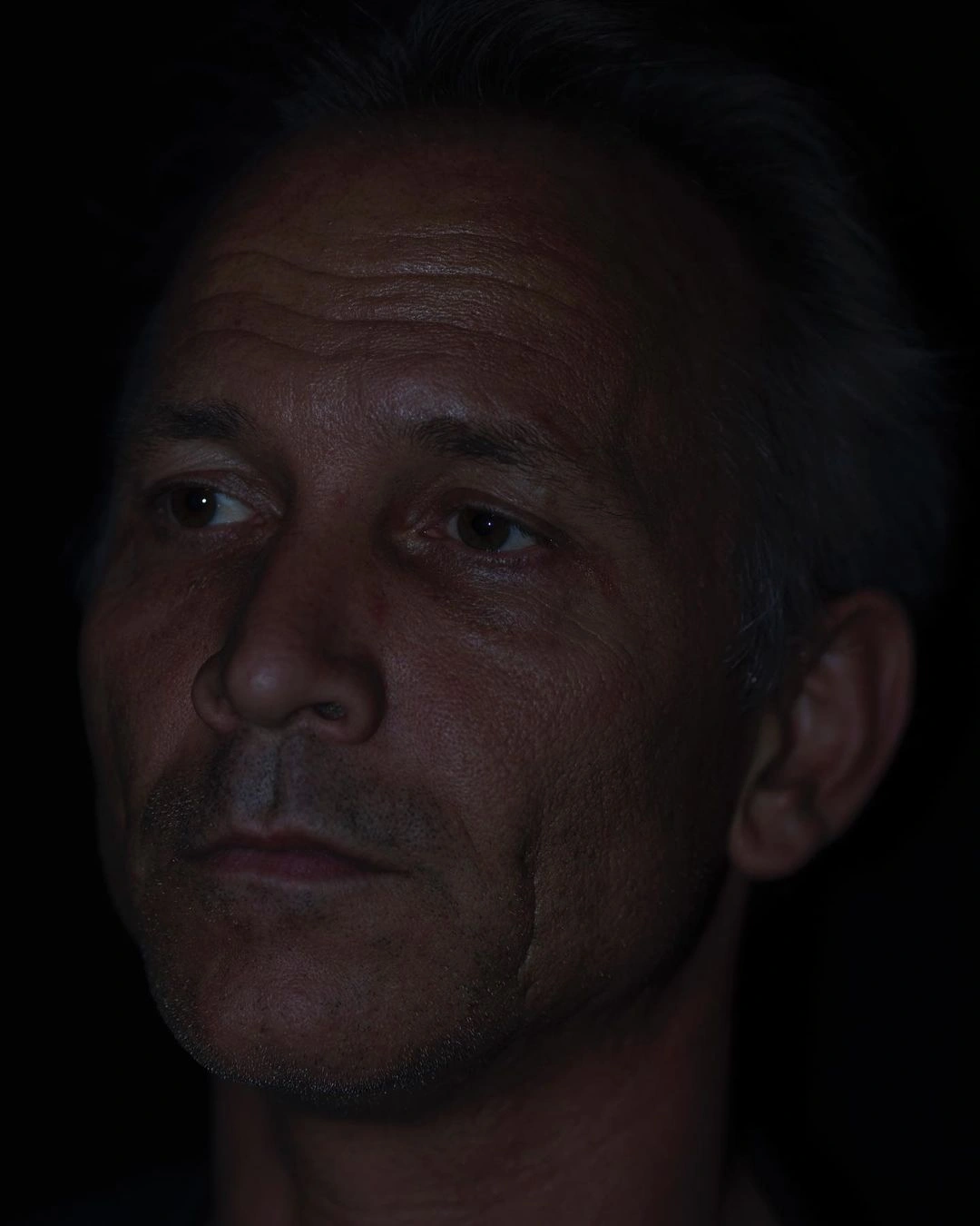 Close-up portrait of a mature man with serious expression against a dark background by photographer Paul Graham