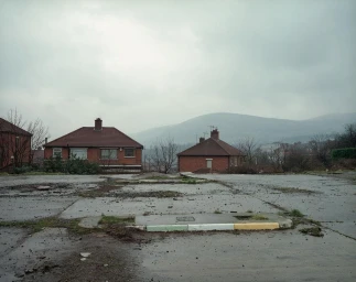 Exterior landscape view of residential brick houses under a heavy overcast sky with distant rolling hills by Paul Graham.