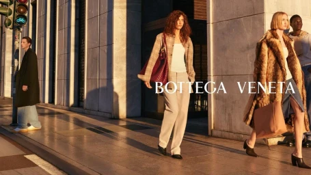 Four models walking along a sunny city sidewalk past large stone building columns during golden hour, photographed by Paul Graham