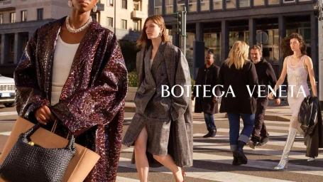 Four models walking across a city street intersection carrying designer handbags and wearing patterned coats.