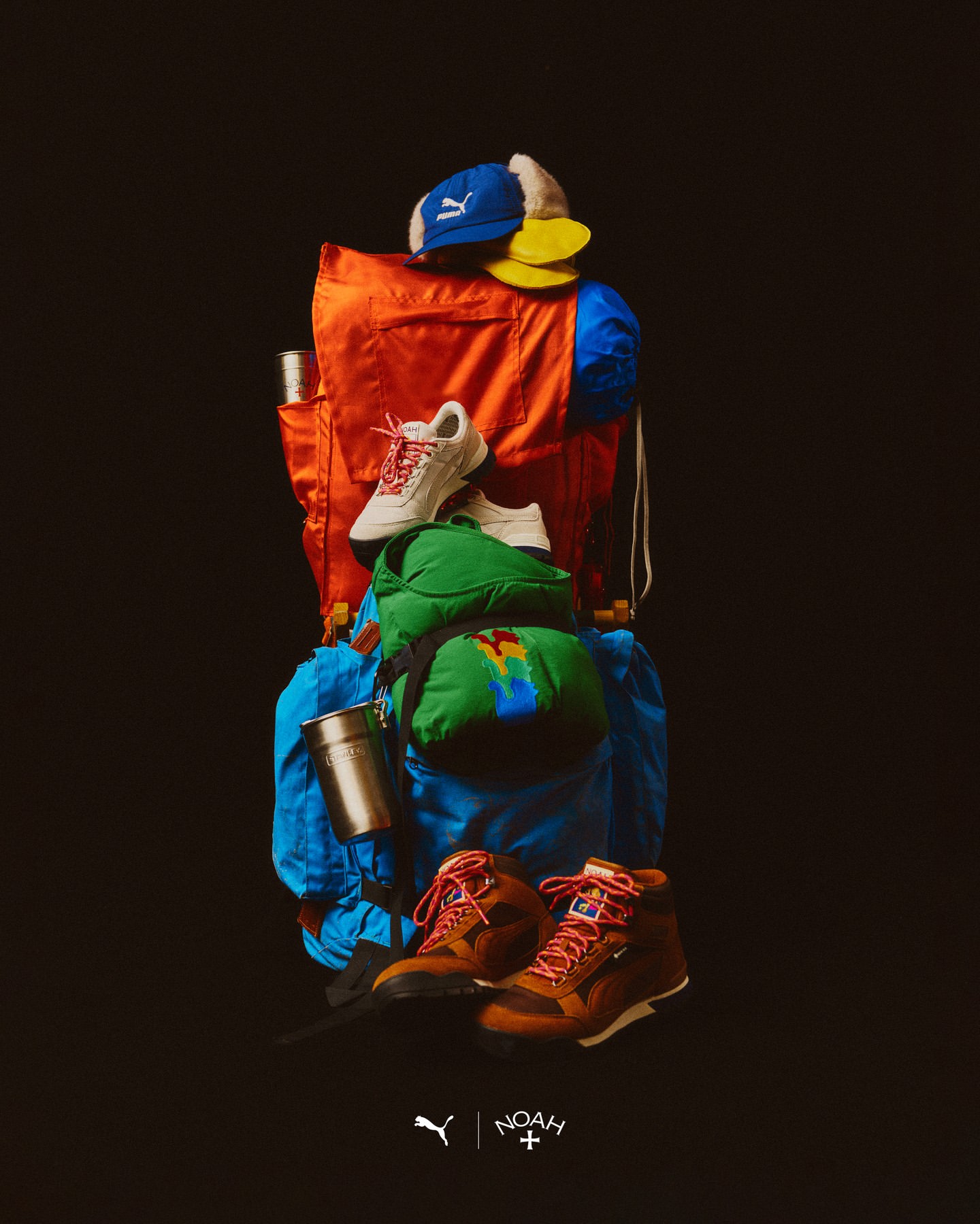 Still life of a vibrant backpack loaded with clothing, hats, water bottle, footwear, and tumbler set against a dark background.