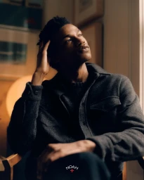 Portrait of a black man wearing a dark grey wool overshirt seated indoors near a window by photographer Paul Hempstead.