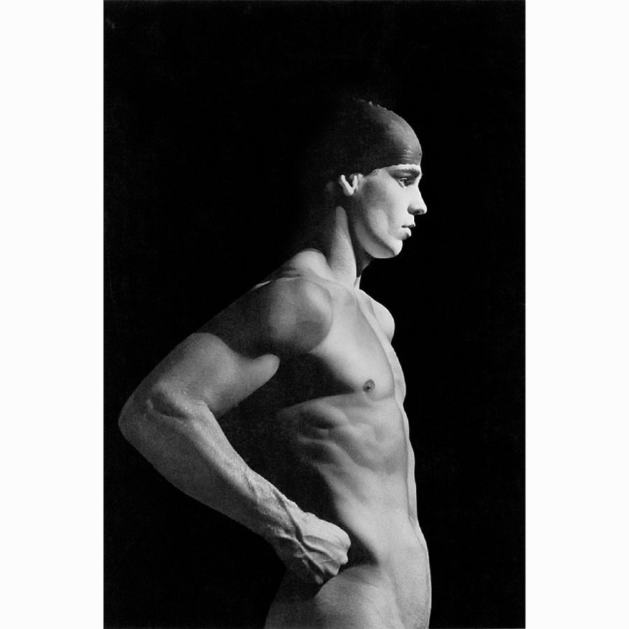 Monochromatic studio portrait of a muscular adult male with a swimming cap looking right against a stark black backdrop.