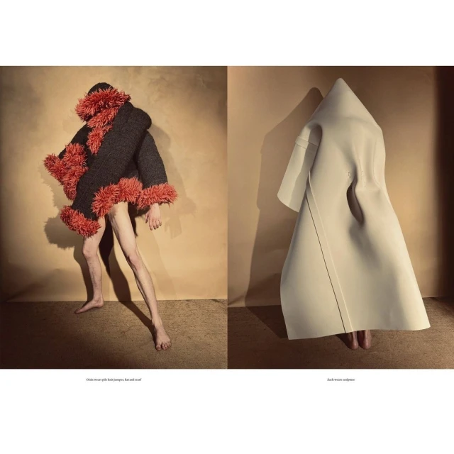 Two figures in avant-garde fashion garments pose in a neutral setting with one figure in a dark furry coat and the other in white garment.