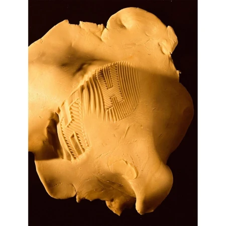 Close-up of soft yellow clay with textured pattern under warm lighting against a dark background, showcasing fine art creation.