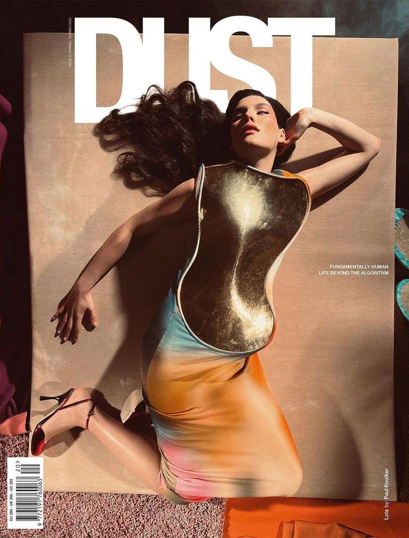 Magazine cover featuring a woman with dark hair lying down wearing a gold corset-like top and tie-dye dress, shot in portrait orientation.