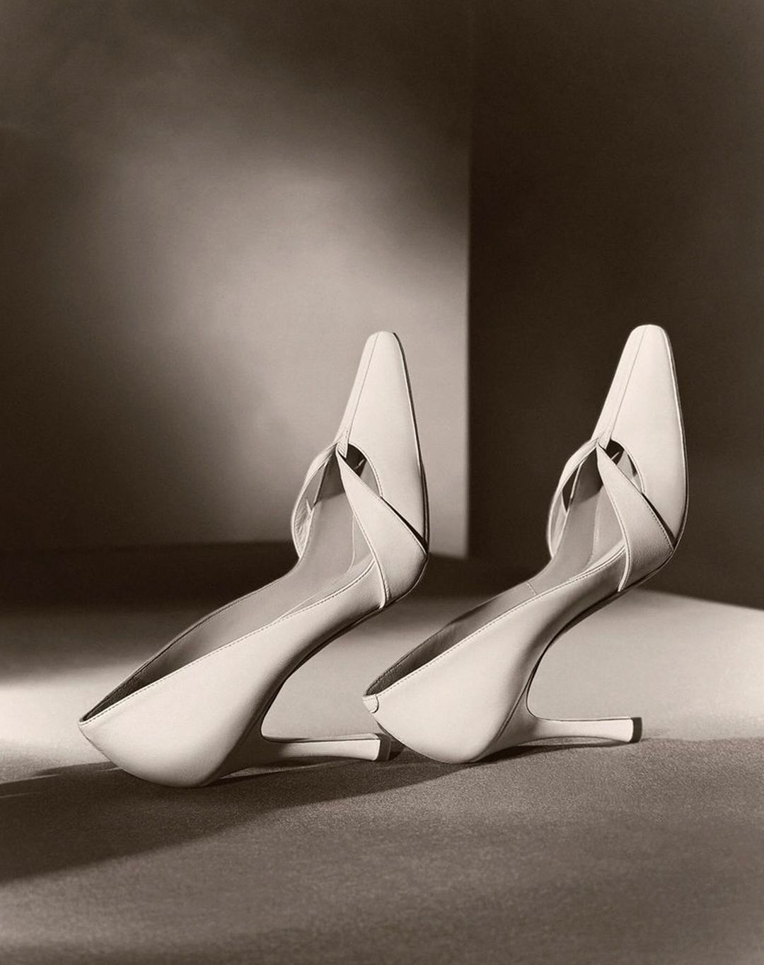 Elegant pair of cream-colored heeled shoes with a pointed toe, staged on a neutral surface in a soft, diffused studio lighting setup.