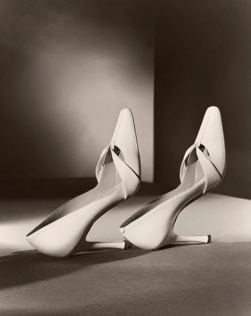 Elegant pair of cream-colored heeled shoes with a pointed toe, staged on a neutral surface in a soft, diffused studio lighting setup.