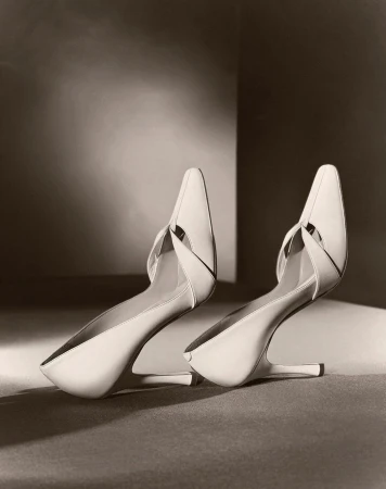 Elegant pair of cream-colored heeled shoes with a pointed toe, staged on a neutral surface in a soft, diffused studio lighting setup.