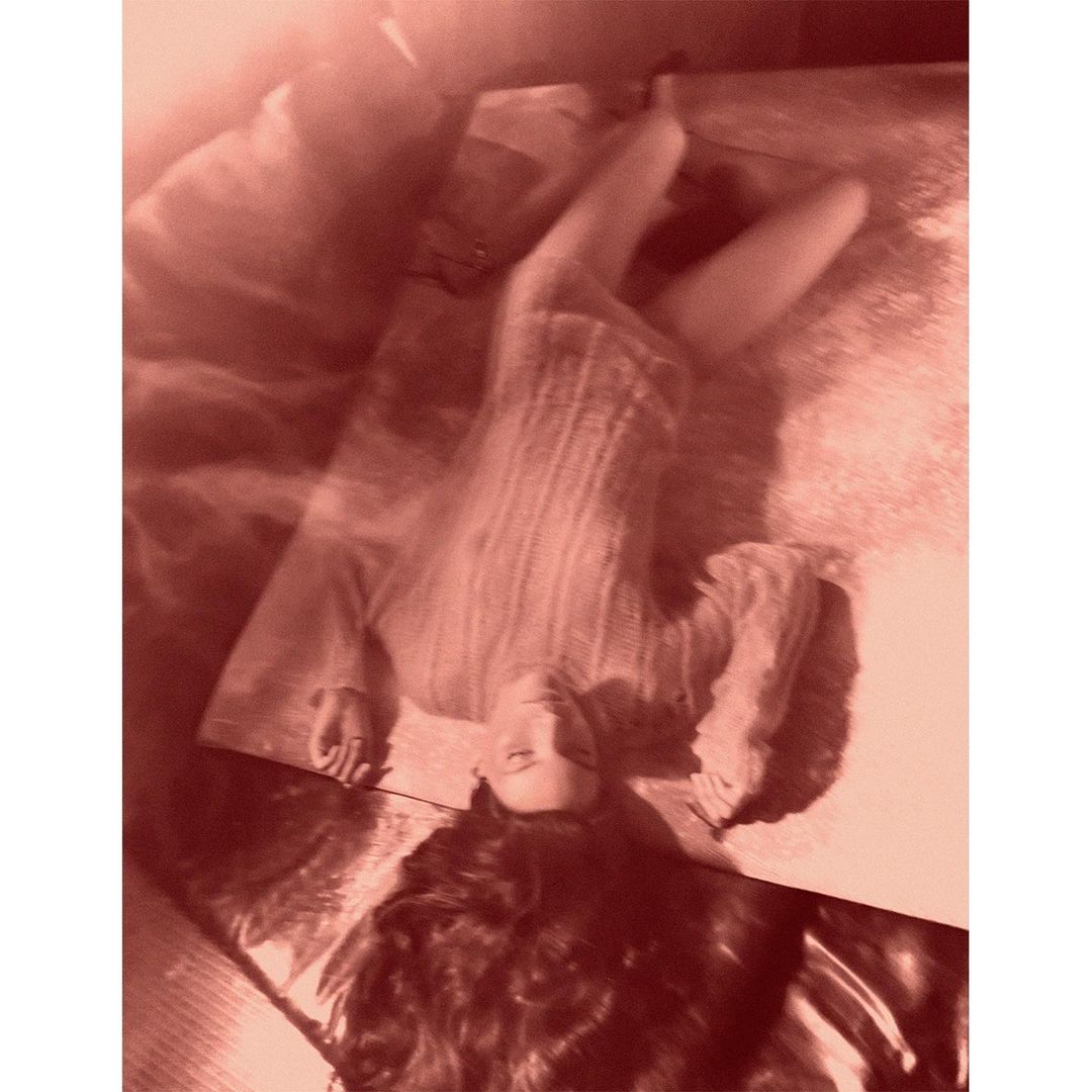 Woman with long hair lies on a mirrored surface indoors, captured in a warm monochrome tone with soft light and a shallow depth of field.