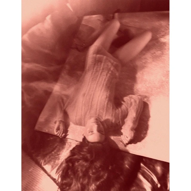 Woman with long hair lies on a mirrored surface indoors, captured in a warm monochrome tone with soft light and a shallow depth of field.