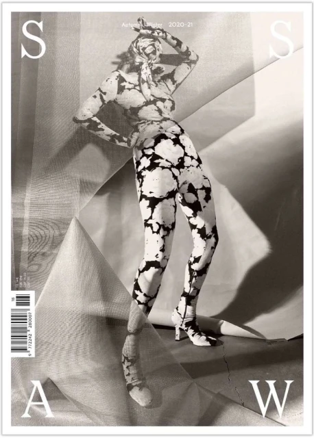 Fashion magazine cover featuring model in black and white patterned leggings and top, against a backdrop of folded fabric.