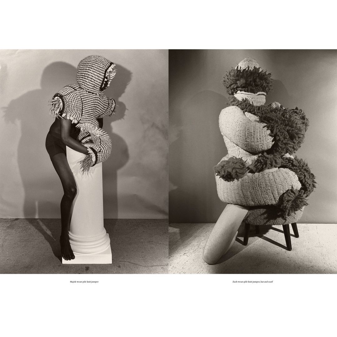 Two figures in unique knitted fashion, one standing on a column, the other seated, in a studio setting with neutral backdrop and soft lighting.