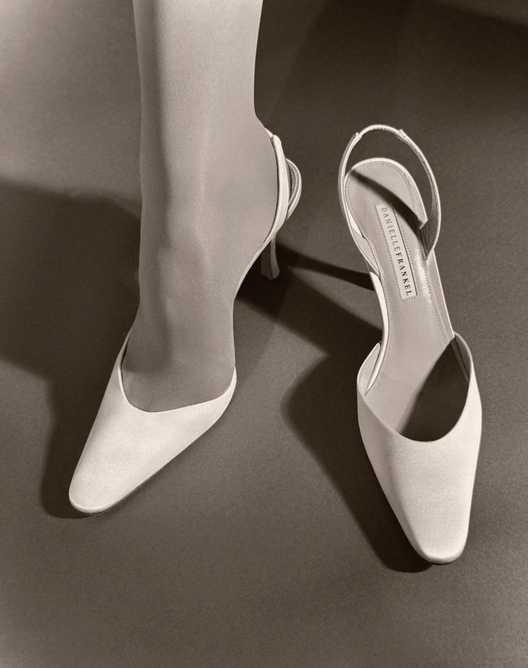 Sepia-toned image of a woman's lower leg and foot in a slingback high heel shoe. Next to it sits another high heel shoe.