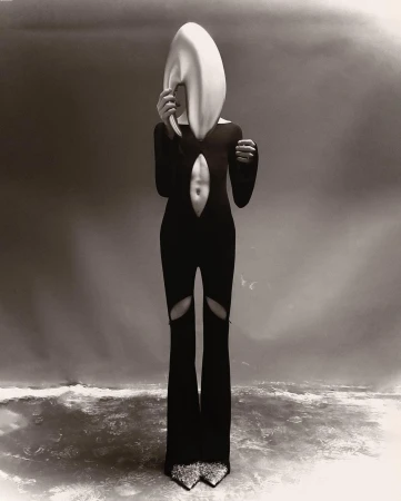 A person in a black bodysuit and statement headpiece poses in front of a gradient background, creating a surreal fashion editorial.