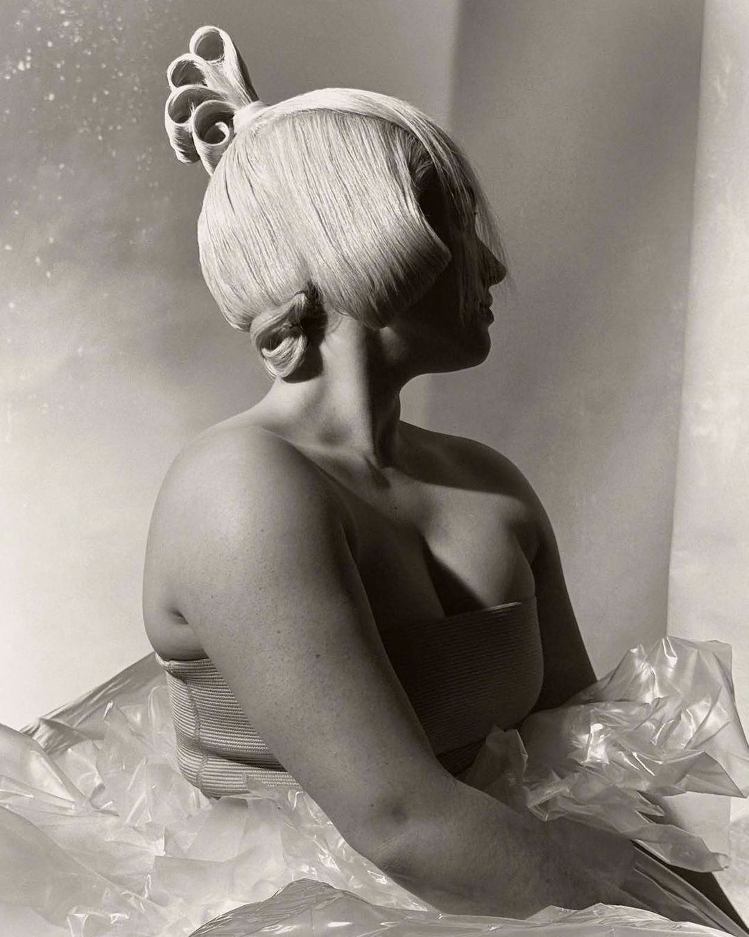 Monochrome portrait of an adult female with an elaborate blonde hairstyle and pale skin, posing in a photo studio with neutral background.