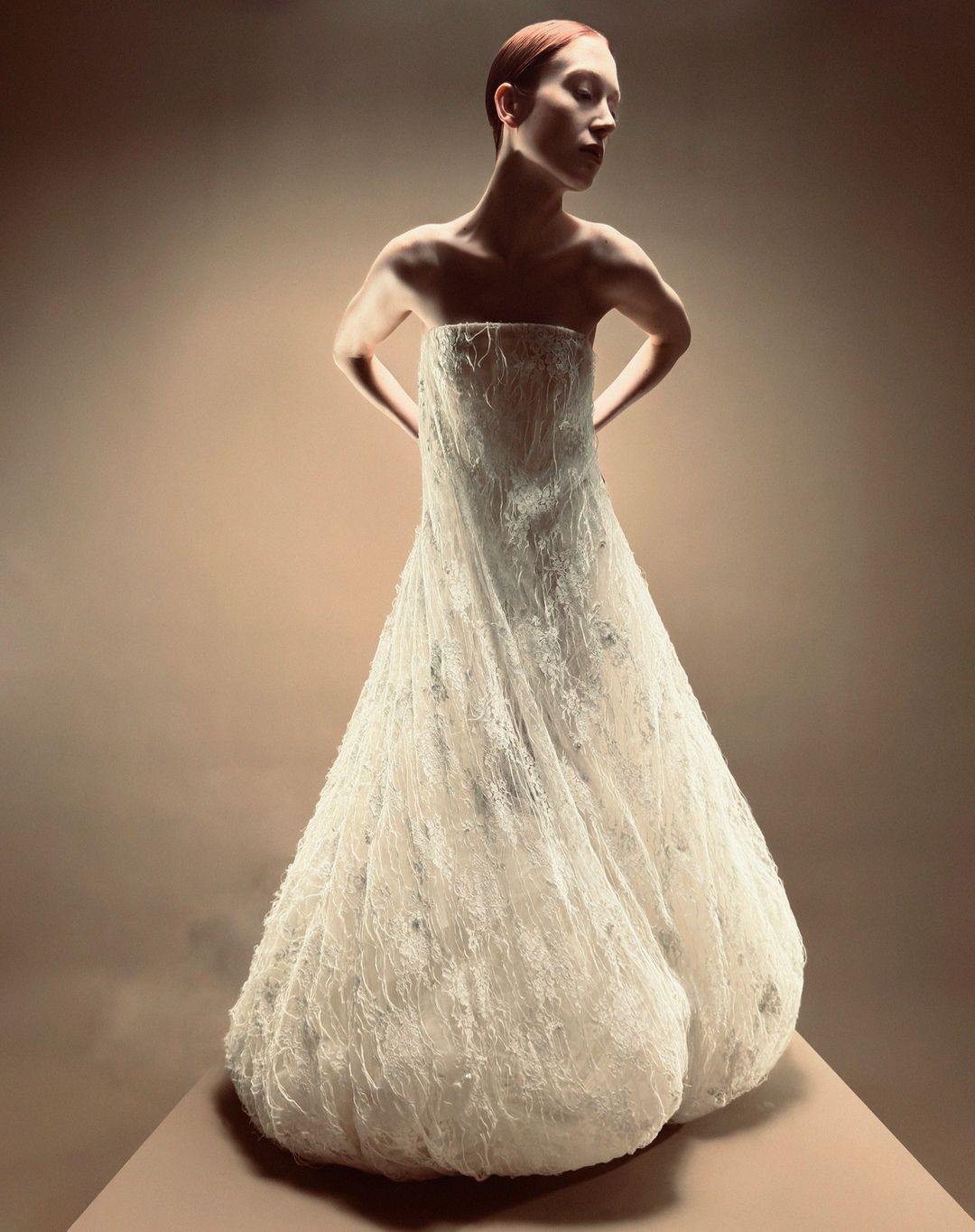 Model in a strapless white textured gown posing against a neutral gradient studio background captured by Paul Kooiker in London.