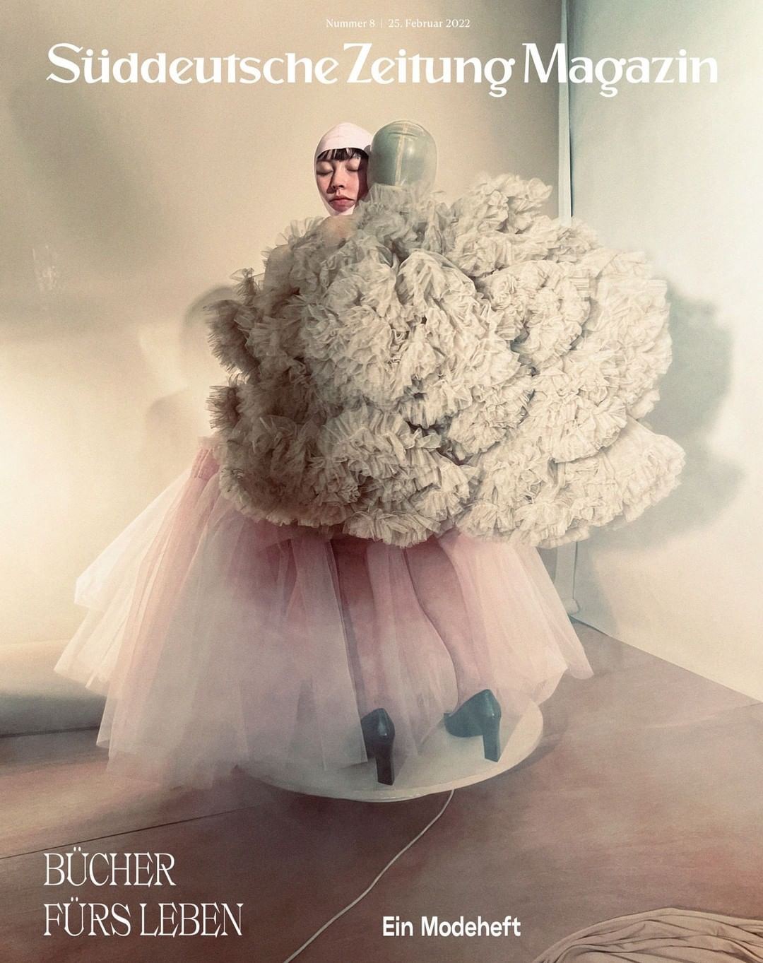 Magazine cover featuring an Asian woman with a unique headpiece, wearing a sculptural ruffled dress with tulle and heels on a turntable.
