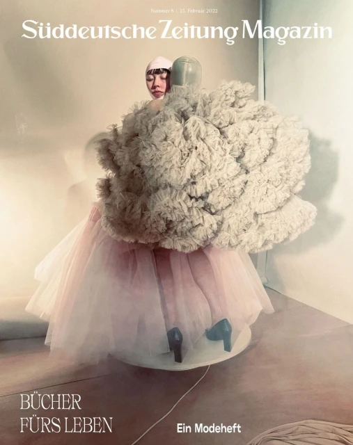 Magazine cover featuring an Asian woman with a unique headpiece, wearing a sculptural ruffled dress with tulle and heels on a turntable.