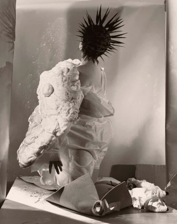 Avant-garde fashion photo: A person in an artful white garment and spiky hair faces away, showcasing unique textures and design in studio setting.