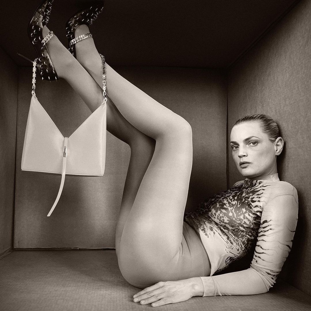 Fashion portrait of an adult female lying in a box with a handbag and designer shoes, sepia-toned, beauty and fashion concept.