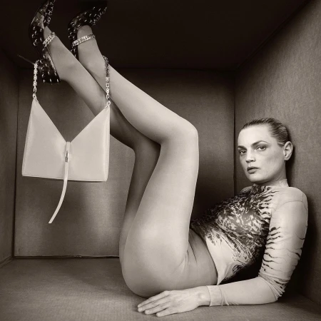 Fashion portrait of an adult female lying in a box with a handbag and designer shoes, sepia-toned, beauty and fashion concept.