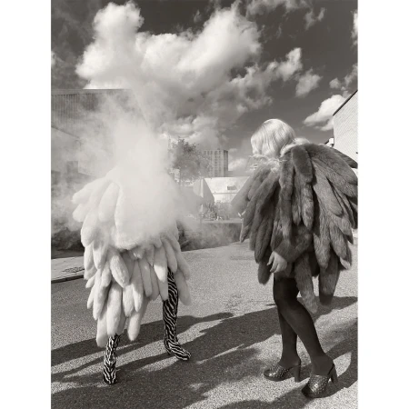 Monochrome outdoor fashion shot of two figures wearing elaborate fluffy clothing on a city street on a cloudy day.