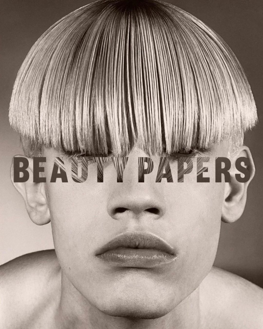 Close-up portrait of a person with a blunt blonde bowl cut hairstyle and the magazine title 'Beauty Papers' layered over the eyes.