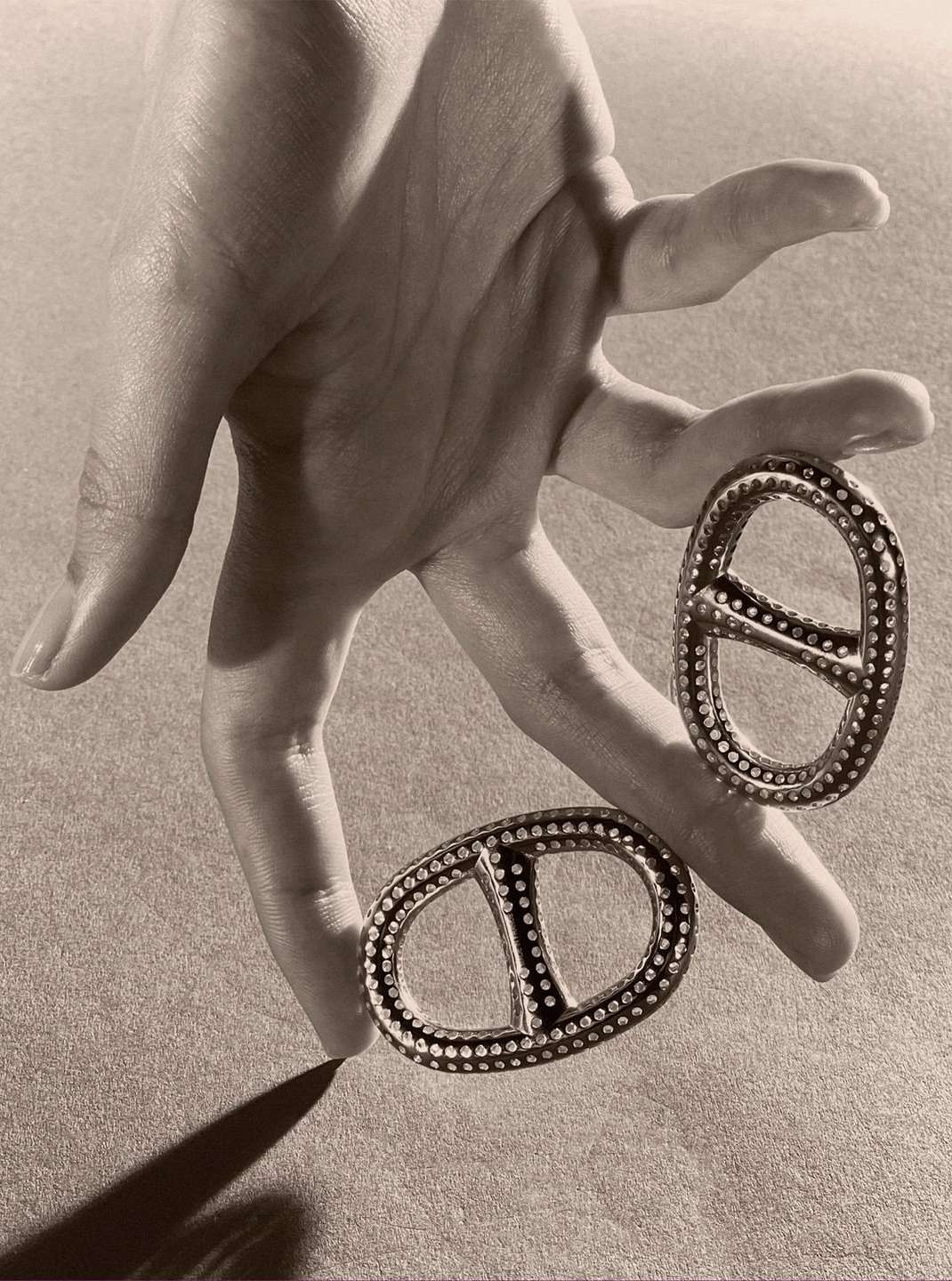 Hand holds two decorative metal ornaments with stud detailing against a neutral background, casting a soft shadow.