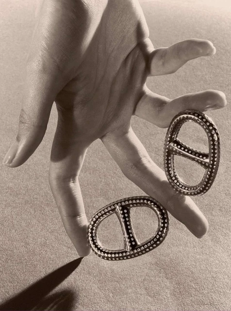 Hand holds two decorative metal ornaments with stud detailing against a neutral background, casting a soft shadow.