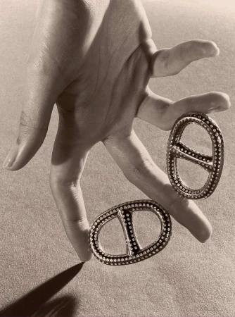 Hand holds two decorative metal ornaments with stud detailing against a neutral background, casting a soft shadow.