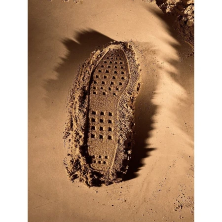 A close-up shows the impression of a shoe sole in sand, filled with a dark brown powder, set against a sandy surface.