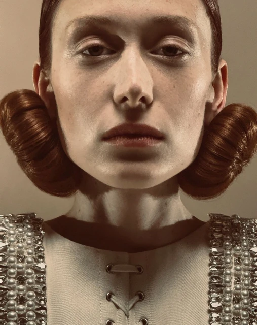 Close-up fashion shot of a fair-skinned adult female with auburn hair styled in rolls, wearing a pearl-embellished white top.