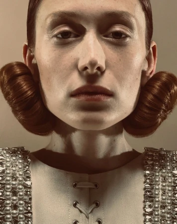 Close-up fashion shot of a fair-skinned adult female with auburn hair styled in rolls, wearing a pearl-embellished white top.