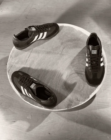 Three Adidas Samba sneakers arranged in a circular pattern on a light wooden surface, showcasing a minimalist shoe display.