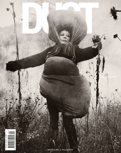 Editorial fashion shot of a woman in field, wearing an oversized fabric garment, with a monochromatic color grade and vintage aesthetic.