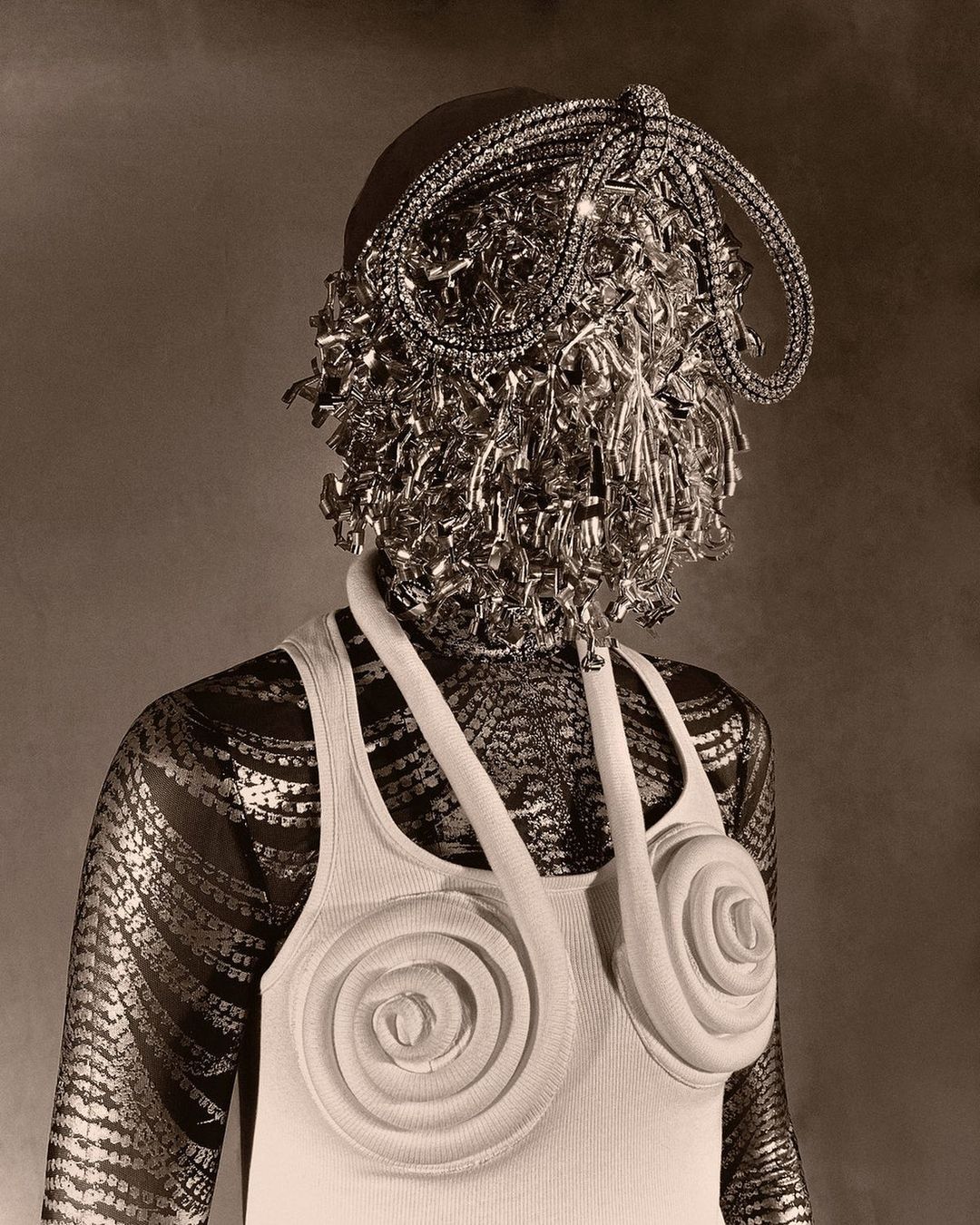 Person with ornate head covering and rose-design top, set against a neutral backdrop in a studio-style fashion shot.