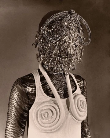 Person with ornate head covering and rose-design top, set against a neutral backdrop in a studio-style fashion shot.