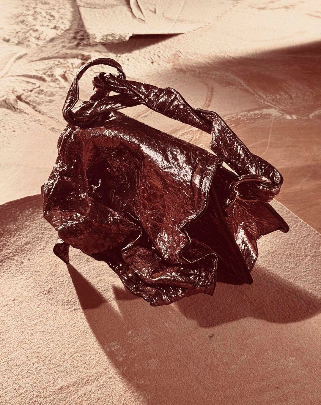 Leather handbag with twisted handle sits on a mottled tan surface in eye-level studio shot with sepia color grading.