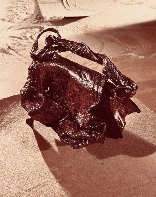 Leather handbag with twisted handle sits on a mottled tan surface in eye-level studio shot with sepia color grading. 