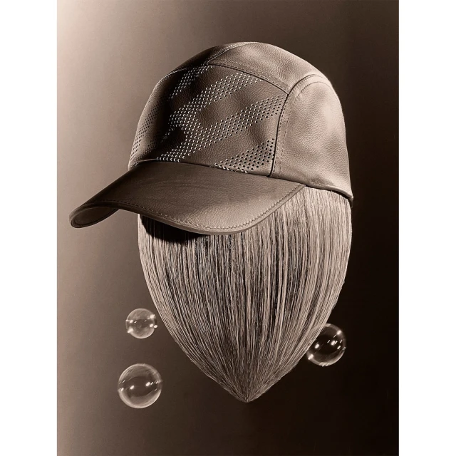 Stylized studio shot of a gray leather baseball cap resting on a sculpture of hair, with three floating bubbles on a gradient backdrop.
