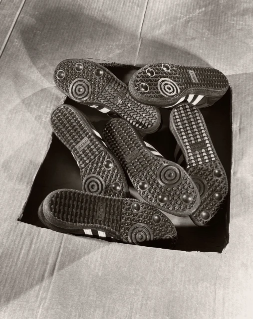 Multiple pairs of Adidas Samba sneakers in a cardboard box, soles facing up, featuring the brand's classic three-stripe design.