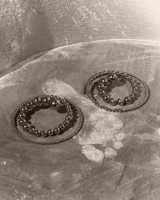 Two silver bead bracelets are coiled on a textured gray surface, creating a simple yet elegant composition in a studio setting.