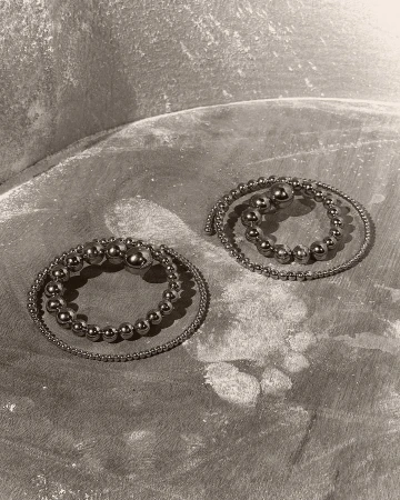 Two silver bead bracelets are coiled on a textured gray surface, creating a simple yet elegant composition in a studio setting.