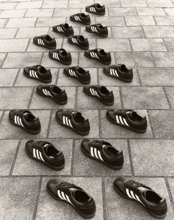 Multiple Adidas sneakers arranged in a pyramid pattern on a brick surface, creating a rhythmic and symmetrical composition, monochrome.