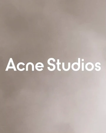 Minimalist studio shot of 'Acne Studios' brand name in bold white sans-serif typeface on a muted beige background with soft gradations.
