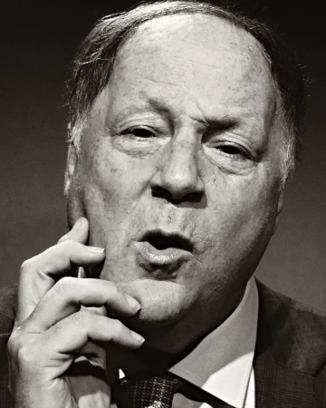 Portrait of an adult man with light skin and dark hair in a suit and tie, holding his hand to his face in a pensive pose.