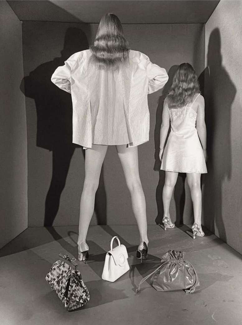 Two models facing a corner in a box set with three handbags on the floor, photographed by Paul Kooiker.
